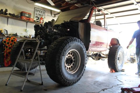 1968 Ford Bronco - A red 1968 Ford Bronco is undergoing modifications in a garage, with its engine exposed and large off-road tires fitted.