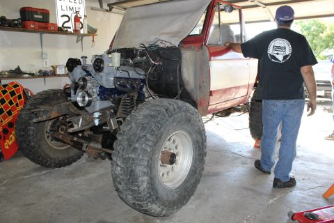 1968 Ford Bronco - A red and white SUV is shown in a garage with its engine exposed and fitted with oversized tires.