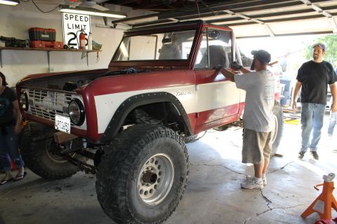 1968 Ford Bronco - A red and white 1968 Ford Bronco is worked on in a garage, with two people observing.