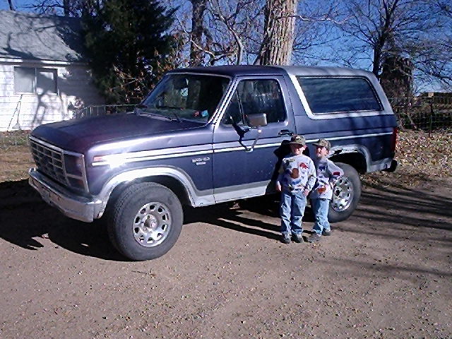Blue Ford Bronco with two kids standing next to it