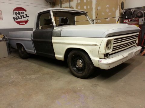 1967 Ford F-100 - This 1967 Ford F-100 pickup truck is in a garage, showing primer gray and black paint, indicating it's undergoing restoration.