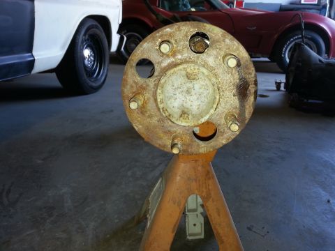 1967 Ford F-100 - A close-up of a rusty wheel hub assembly is shown, with parts of a white truck and a red car visible in the background.