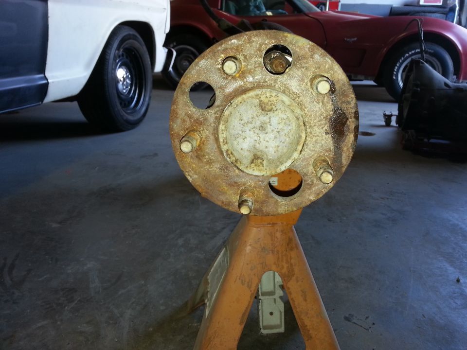 Rusted wheel hub assembly on orange jack stand, white truck side and red car in background