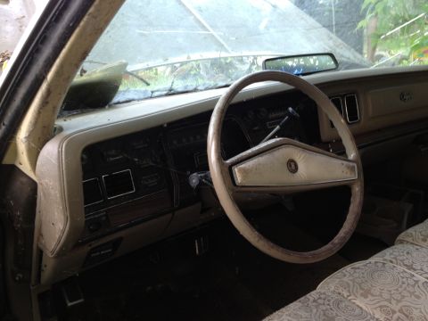 1988 Ford Bronco - The interior of a vintage car shows a worn dashboard, steering wheel, and patterned seat fabric.