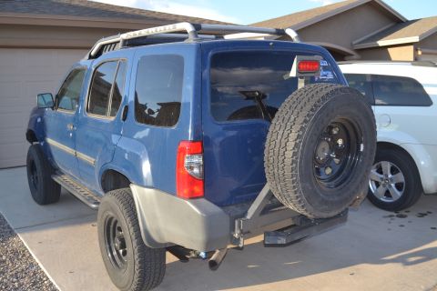 2004 Nissan Xterra - The rear-left view of a blue 2004 Nissan Xterra shows its roof rack and spare tire.