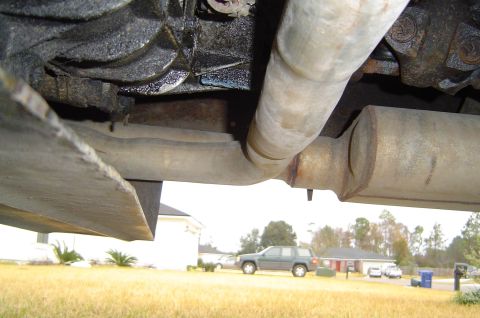 1993 Ford Bronco - The underside of a vehicle's exhaust system is visible, with a dark SUV parked in the background.