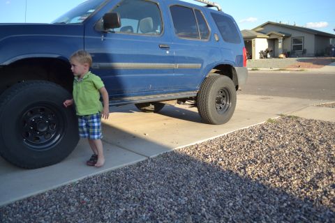 2004 Nissan Xterra - A blue 2004 Nissan Xterra is parked on a driveway with a young child standing beside the large front tire.