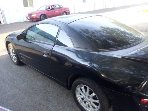 2001 Mitsubishi Eclipse - A black coupe is parked in front of a building with a red sedan in the background.