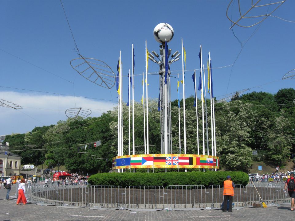 Monument with flags and a soccer ball on top, surrounded by metal barriers and trees