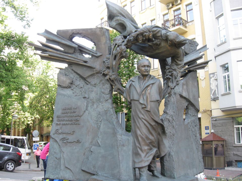 Monumental sculpture of a man and abstract shapes, with a bus and car in the background