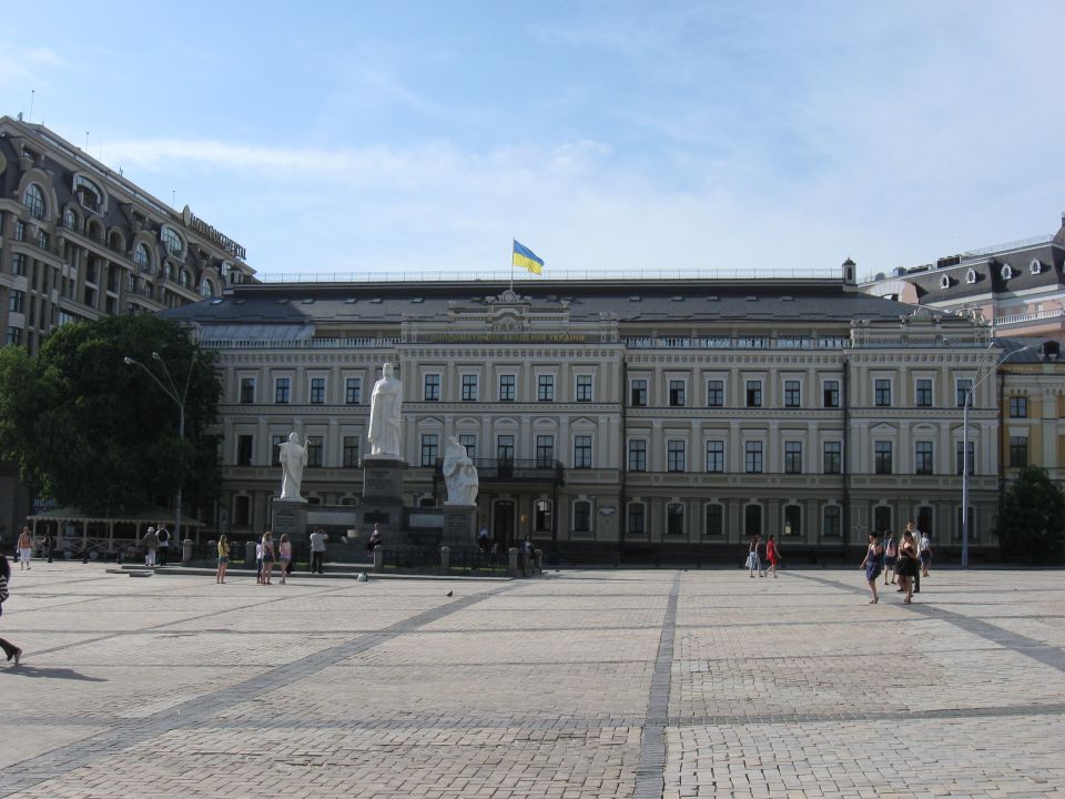 Large building with statues in a plaza, Ukrainian flag on top