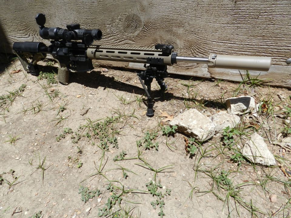 Rifle with scope, bipod, and suppressor resting on the ground
