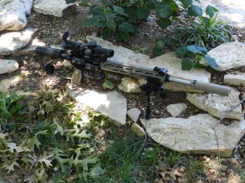 1996 Ford Bronco - An assault rifle with a scope and bipod rests on a bed of rocks and grass.