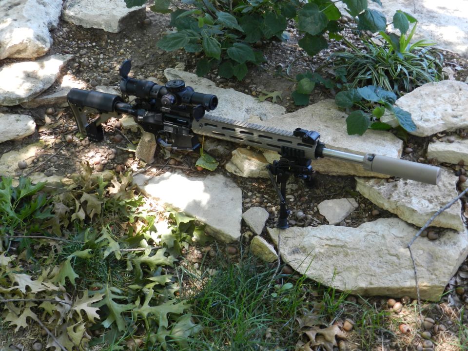 Assault rifle with scope and bipod on rocks and grass