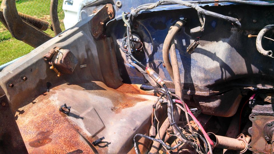 Engine bay with rust and exposed wiring. Some hoses and metal components are visible