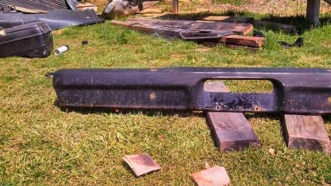 1979 Ford Bronco - A black bumper, likely from an older vehicle, is displayed outdoors on a grassy area.