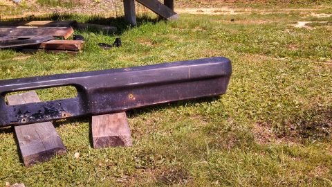 1979 Ford Bronco - A dark front bumper, likely from an older vehicle, is shown outdoors resting on wooden blocks.