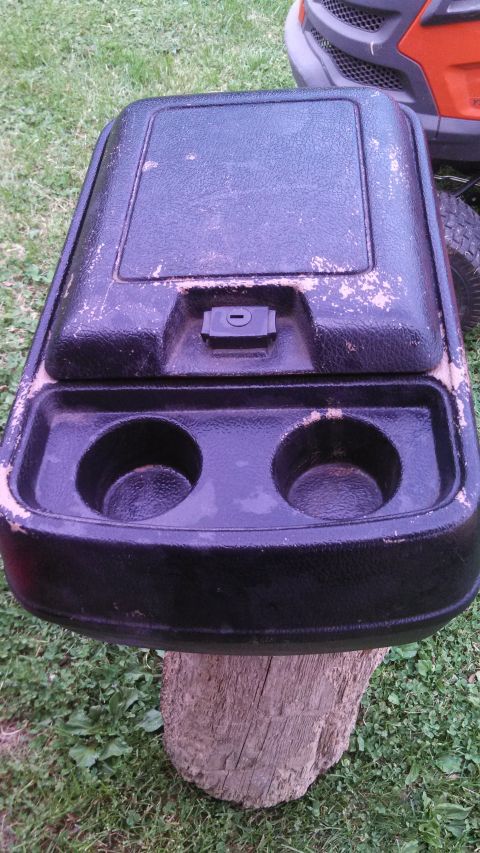 1979 Ford Bronco - A worn black center console with cup holders and a lock is displayed outdoors.