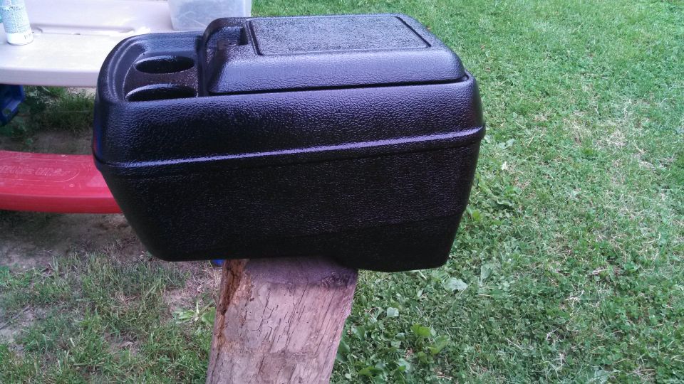 Black plastic center console with two cup holders and a lidded compartment