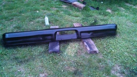 1979 Ford Bronco - A black bumper is shown outdoors, resting on wooden supports.