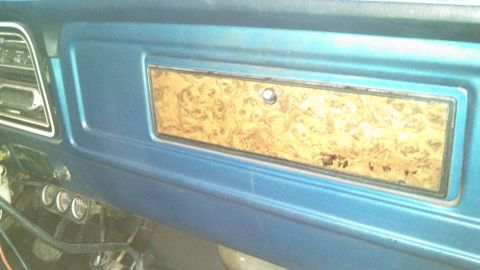 1979 Ford Bronco - The interior of a 1979 Ford Bronco shows a blue dashboard with a wood grain trim accent panel and visible gauges below.