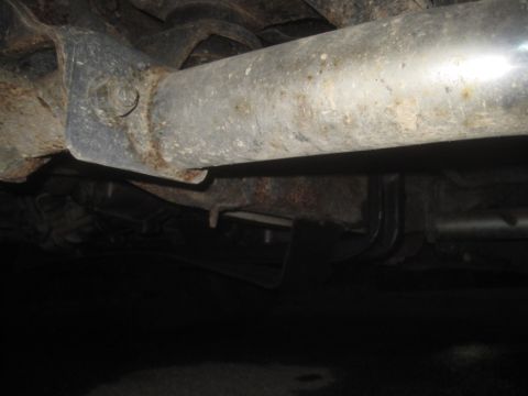 1993 Ford Bronco - The underside of a vehicle shows significant rust and a large metal pipe.