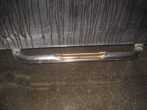 1993 Ford Bronco - A close-up of a damaged chrome running board against a dark, wet background.