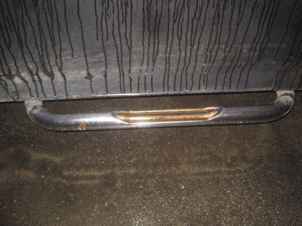Chrome running board with rust and dents on a dark surface with water streaks