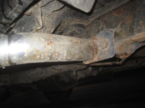 1993 Ford Bronco - The underside of a vehicle displays significant rust on its frame and exhaust system components.