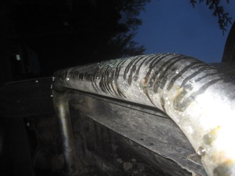 1993 Ford Bronco - The underside of a vehicle shows a corroded exhaust pipe with water droplets and black residue.