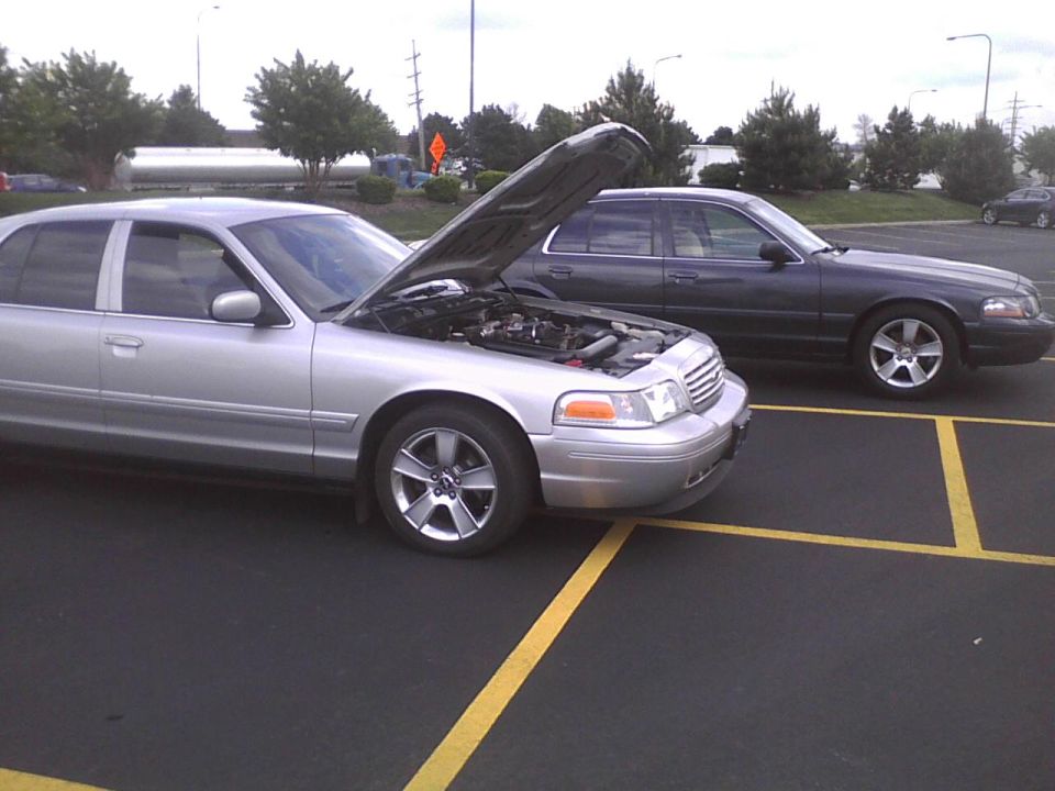 Silver 2003 Ford Crown Victoria with hood open, parked next to a dark gray 2003 Ford Crown Victoria