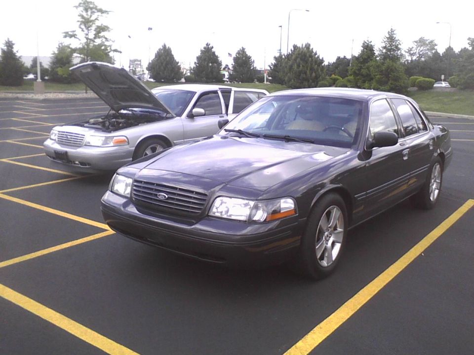 Two Ford Crown Victorias parked in a lot, one with the hood open