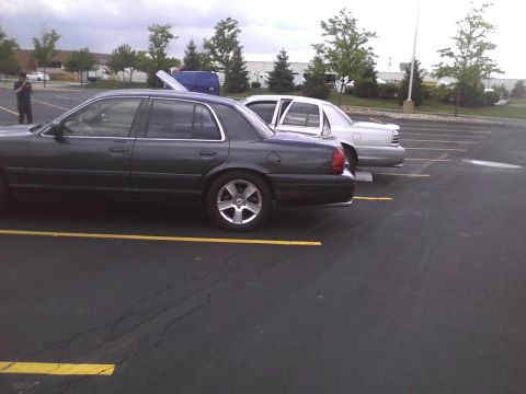 2003 Ford Crown Victoria - Two sedans are parked in a lot under an overcast sky.