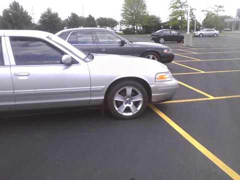 2003 Ford Crown Victoria - A silver sedan is parked in a lot next to a dark sedan.