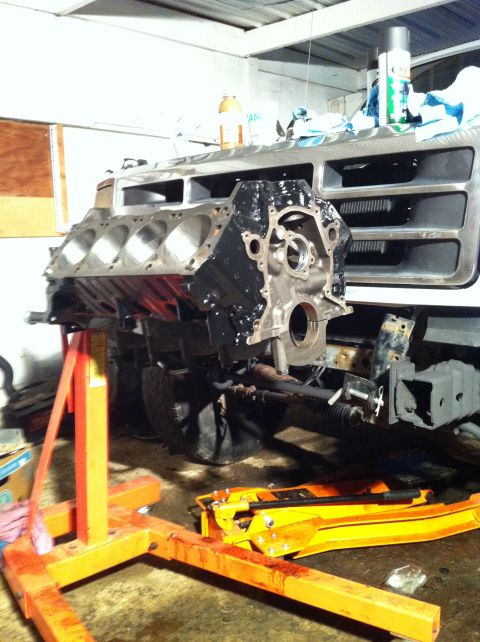 1992 Ford Bronco - An engine block is supported by an engine hoist in front of a vehicle's front end, suggesting a repair or rebuild.