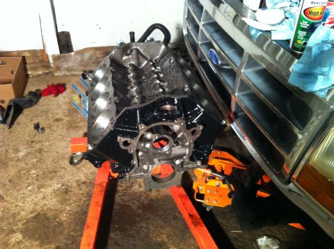 1992 Ford Bronco - A freshly painted engine block sits on a stand, positioned beside the front end of a truck. Cleaning supplies are visible on the truck's gr…