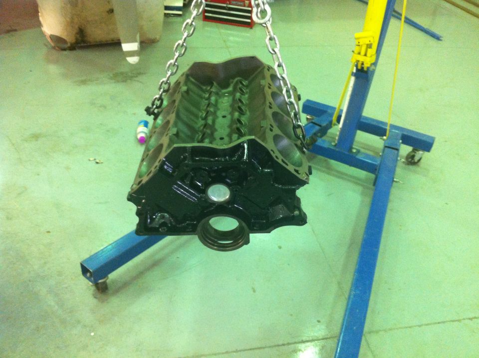Black engine block suspended by chains over a blue engine stand