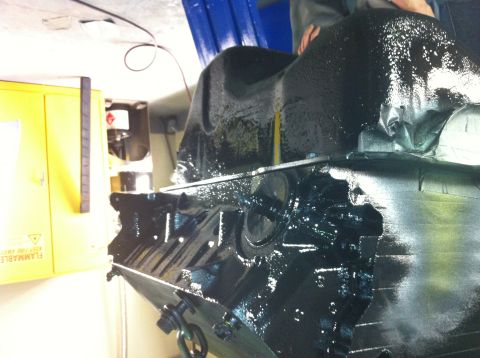 1992 Ford Bronco - Close-up of a black painted engine part, possibly a transmission or oil pan, with visible bolts and a chain loop attached.