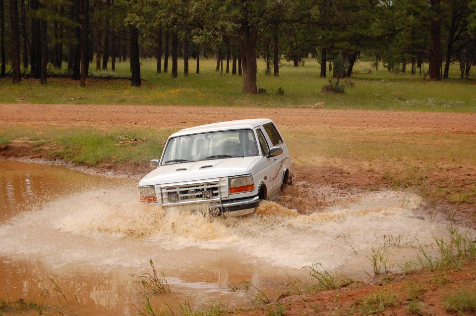 White 1996 Ford Bronco splashing through a muddy water obstacle
