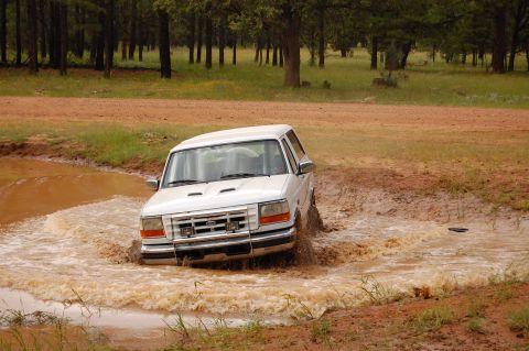 1996 Ford Bronco - White Ford Bronco navigates a muddy obstacle course in a wooded area.
