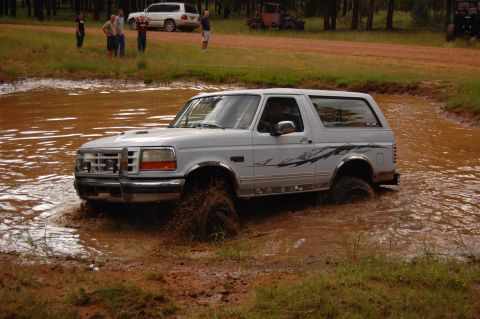 1996 Ford Bronco - White 1996 Ford Bronco navigates a muddy obstacle course, with spectators in the background.