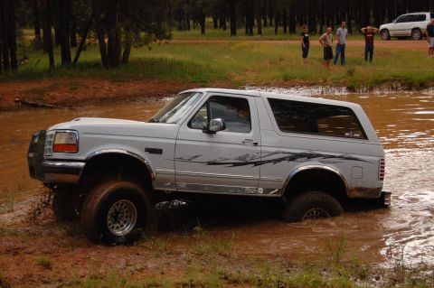 1996 Ford Bronco - White 1996 Ford Bronco navigating a muddy off-road course with spectators nearby.