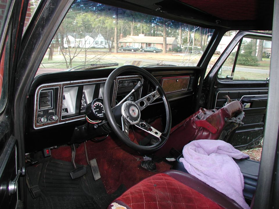 1979 Ford Bronco interior with chrome steering wheel, aftermarket tach, woodgrain dash and red bench seat