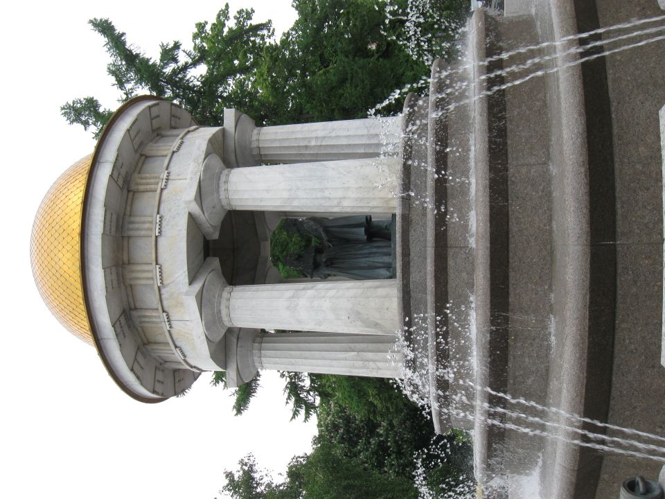 Monumental fountain with a golden dome, marble columns, and a statue inside. Water sprays from the tiered structure