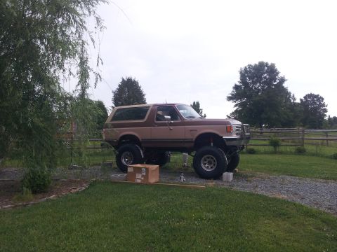 1988 Ford Bronco - This lifted 1988 Ford Bronco is parked outdoors on a gravel driveway with a wooden fence in the background.