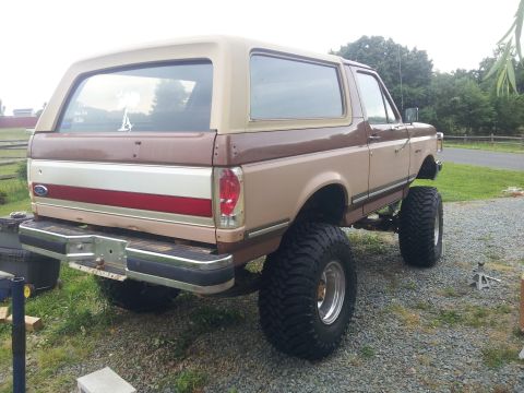 1988 Ford Bronco - This lifted Ford Bronco has a two-tone paint job and oversized tires, seen from the rear.