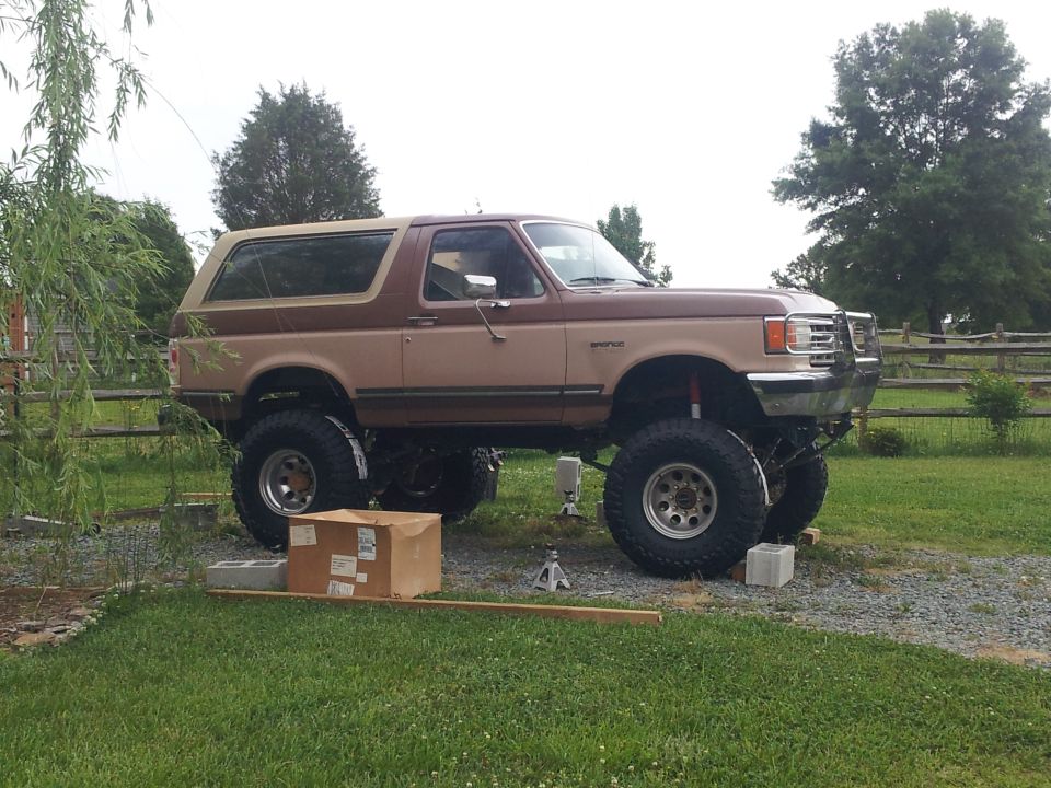 Brown lifted Ford Bronco on cinder blocks with a jack, side view
