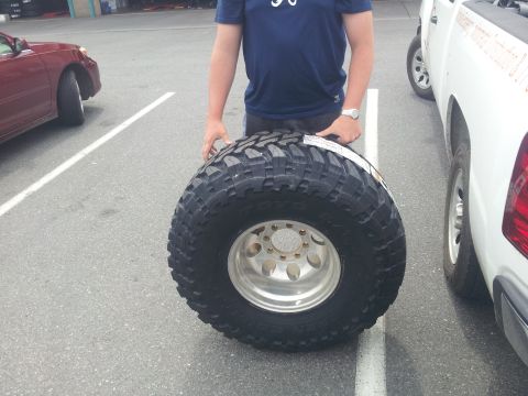 1988 Ford Bronco - A person holds a large off-road tire and wheel next to a white pickup truck.