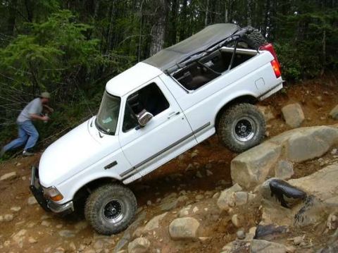 1995 Ford Bronco - This white SUV is navigating a challenging rocky terrain on a wooded trail.