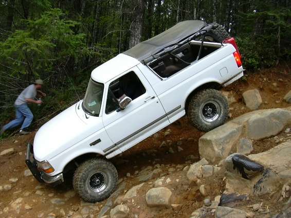 White Ford Bronco climbing rocks on a wooded off-road trail